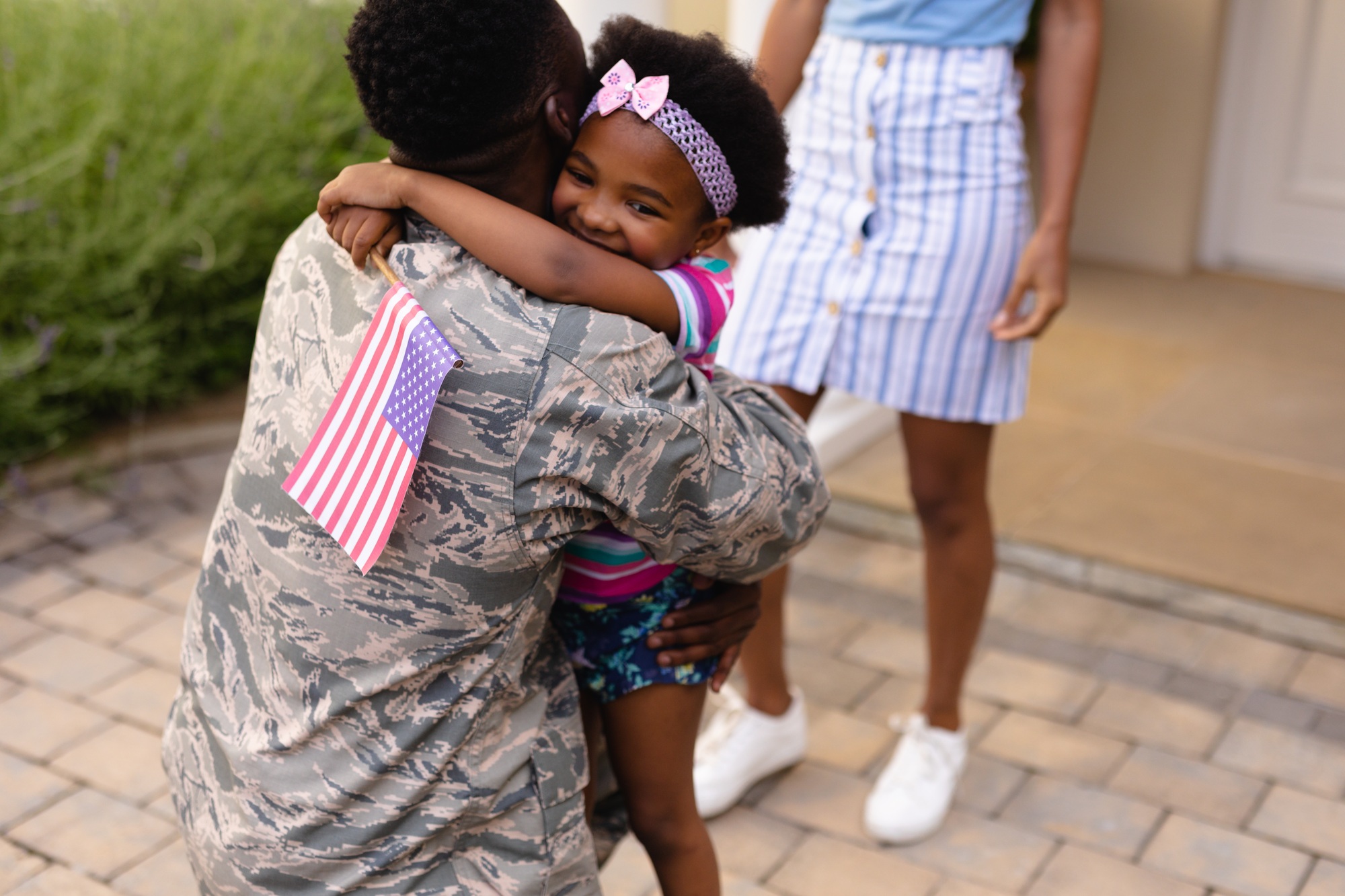 Army soldier embracing african american girl with usa flag at house entrance