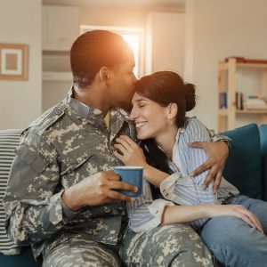 Happy African American Male Soldier In Military Uniform and His Wife Enjoying One Another after returning home from service while sitting on the sofa in the living room. Homecoming, Reunion, Returning Home to Family and Happiness Concept