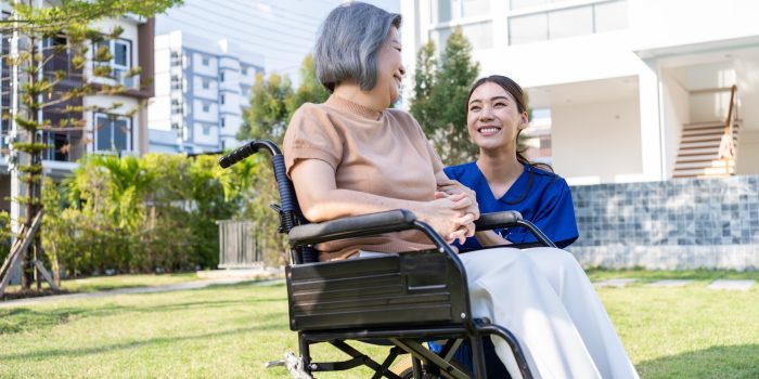 Asian happy senior woman patient sitting on wheelchair at green park.